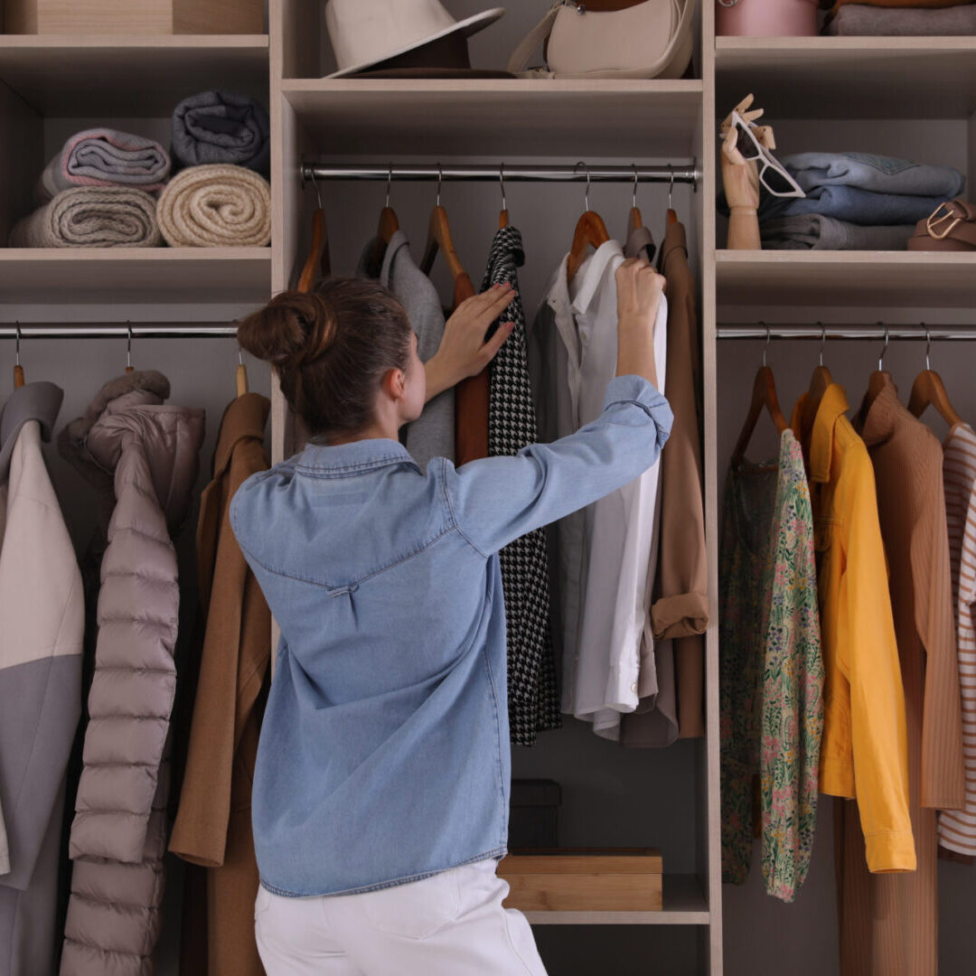 A woman is reaching for some clothes in her closet.